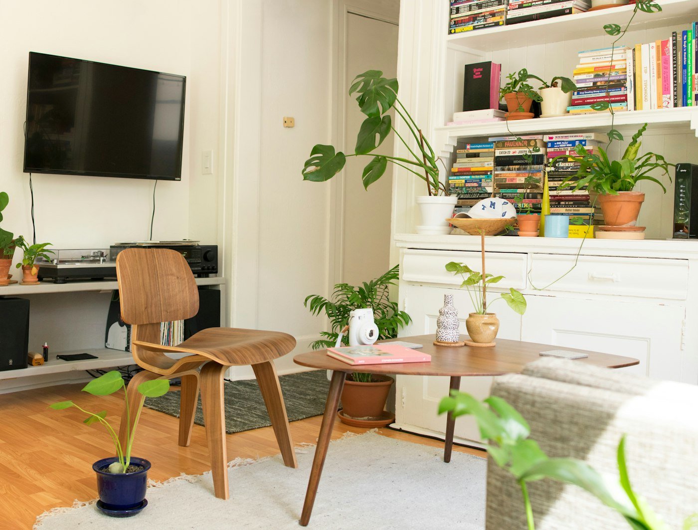 A wooden chair, a low table, bookshelves full of books, and houseplants around a television
