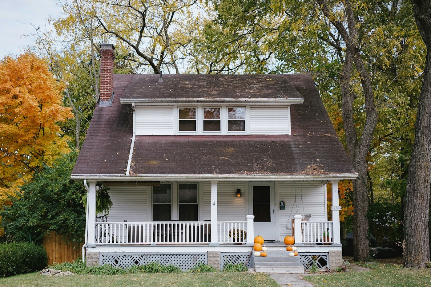 A white house with a porch, pumpkins on the step, and trees turning yellow